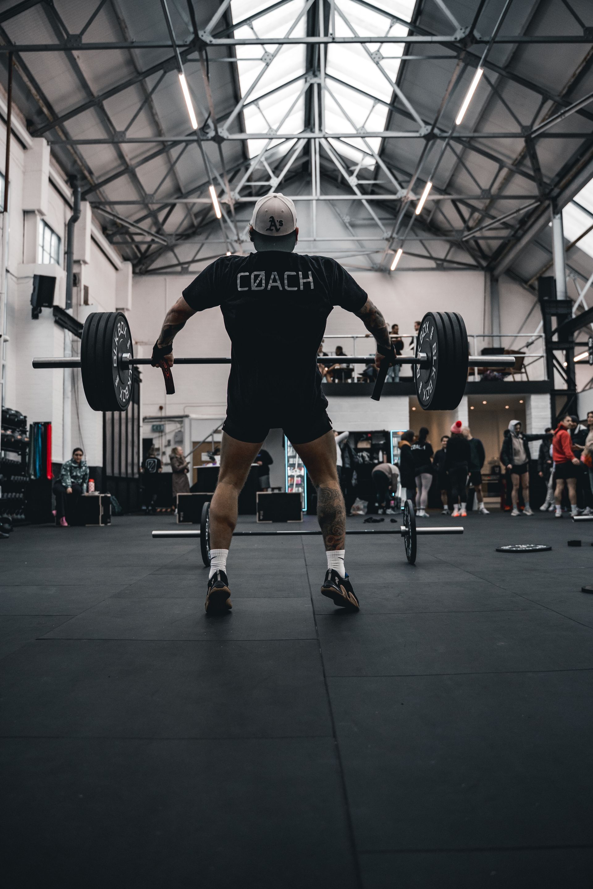 Weightlifter in black holding a barbell in a gym with spectators and equipment.