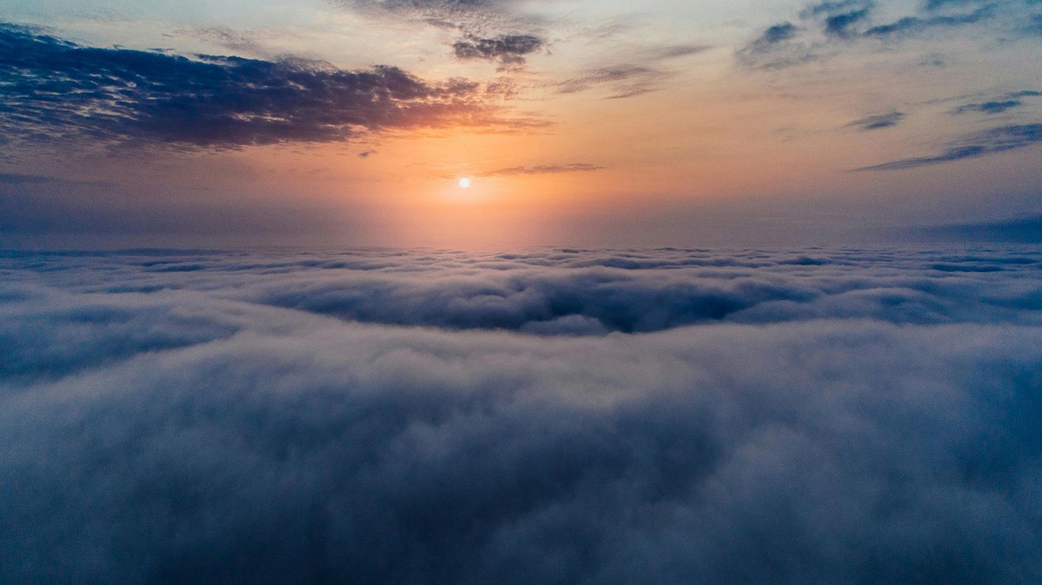 Sunrise over a sea of clouds; orange and blue hues.