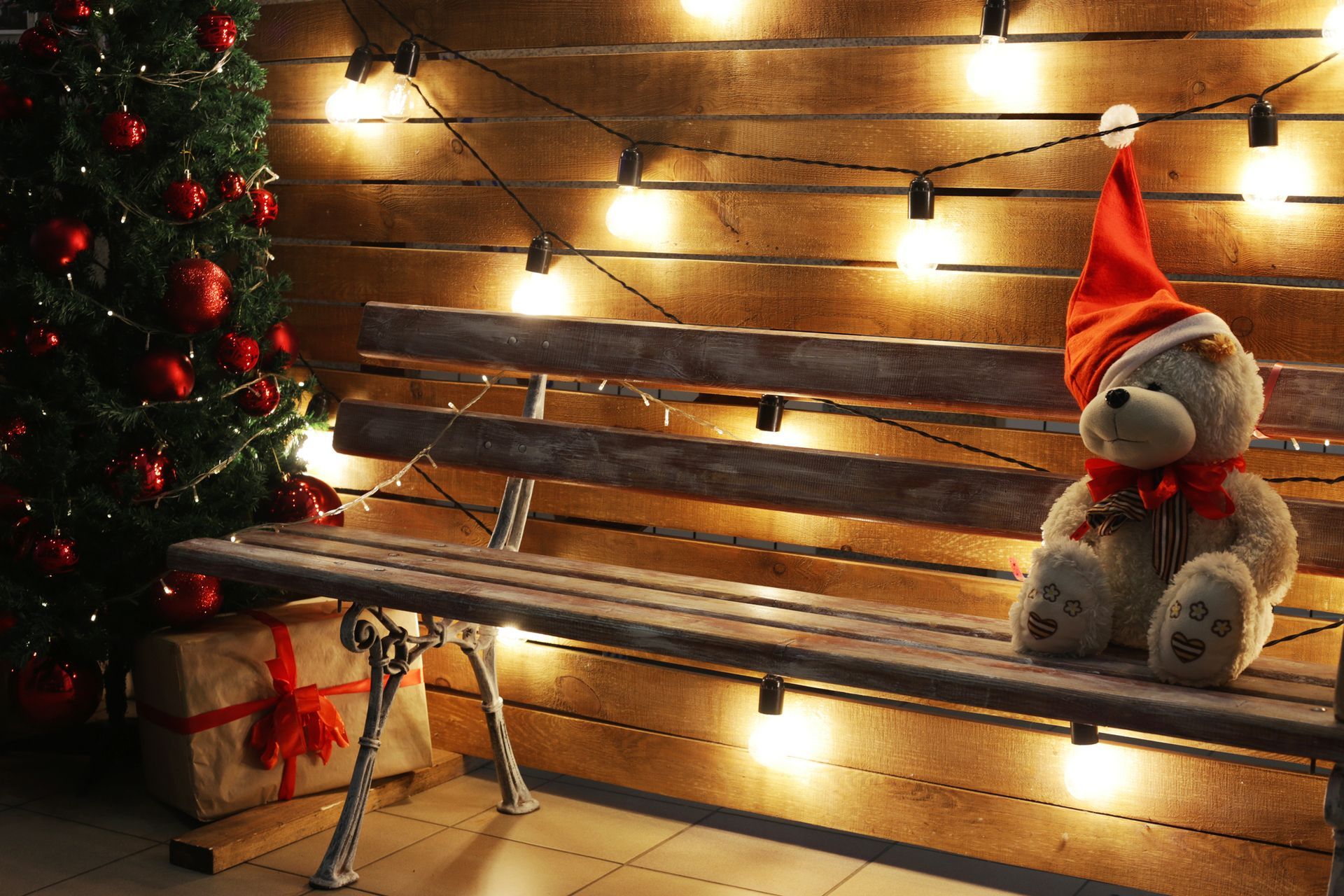 Teddy bear sitting alone on a bench next to a Christmas tree 