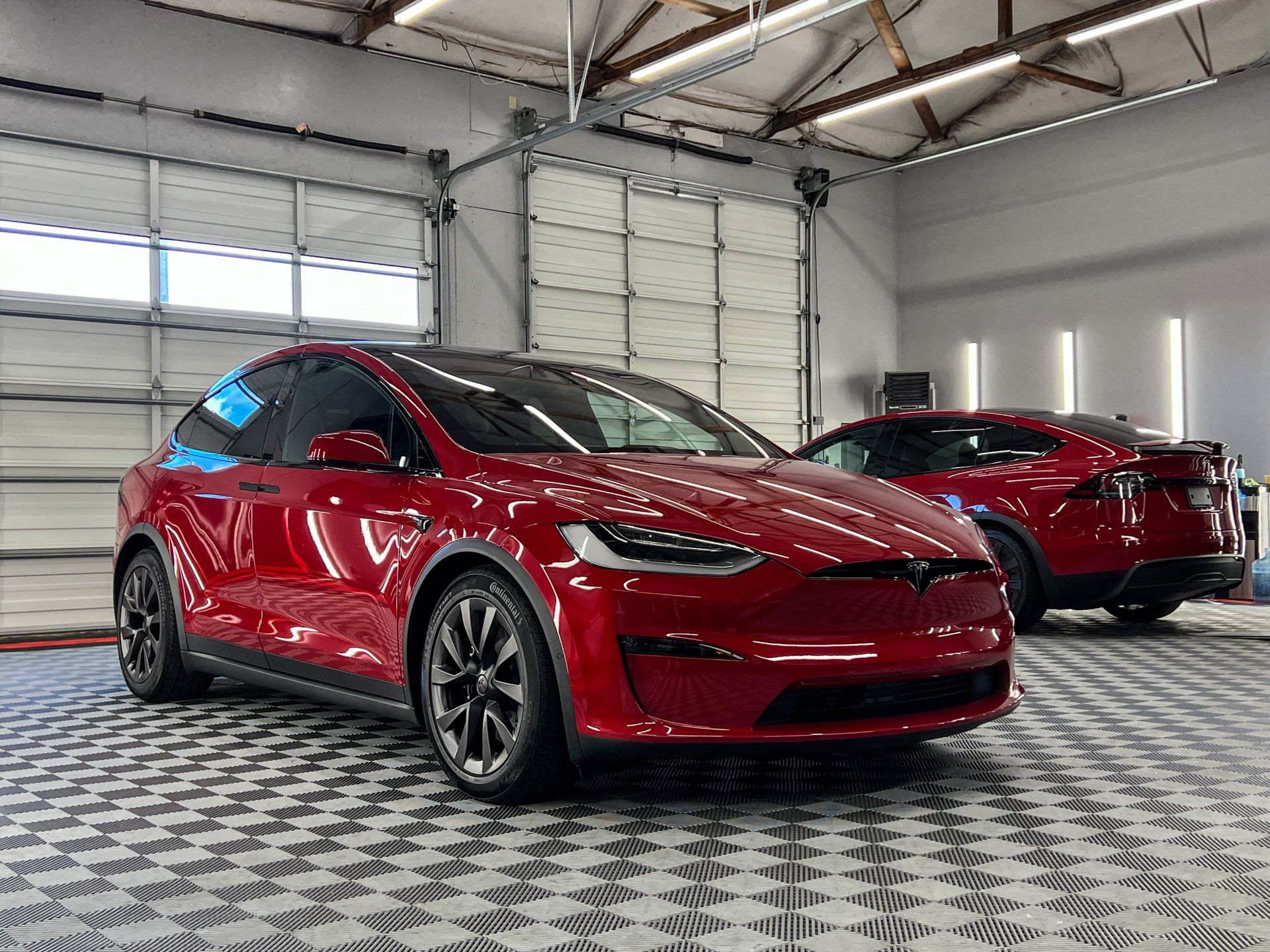 Two red tesla model xs are parked in a garage.