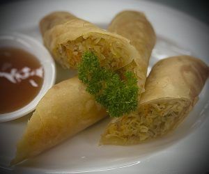 A plate of spring rolls with dipping sauce on a table.