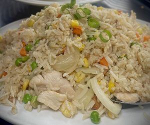 A plate of fried rice with chicken and vegetables on a table.