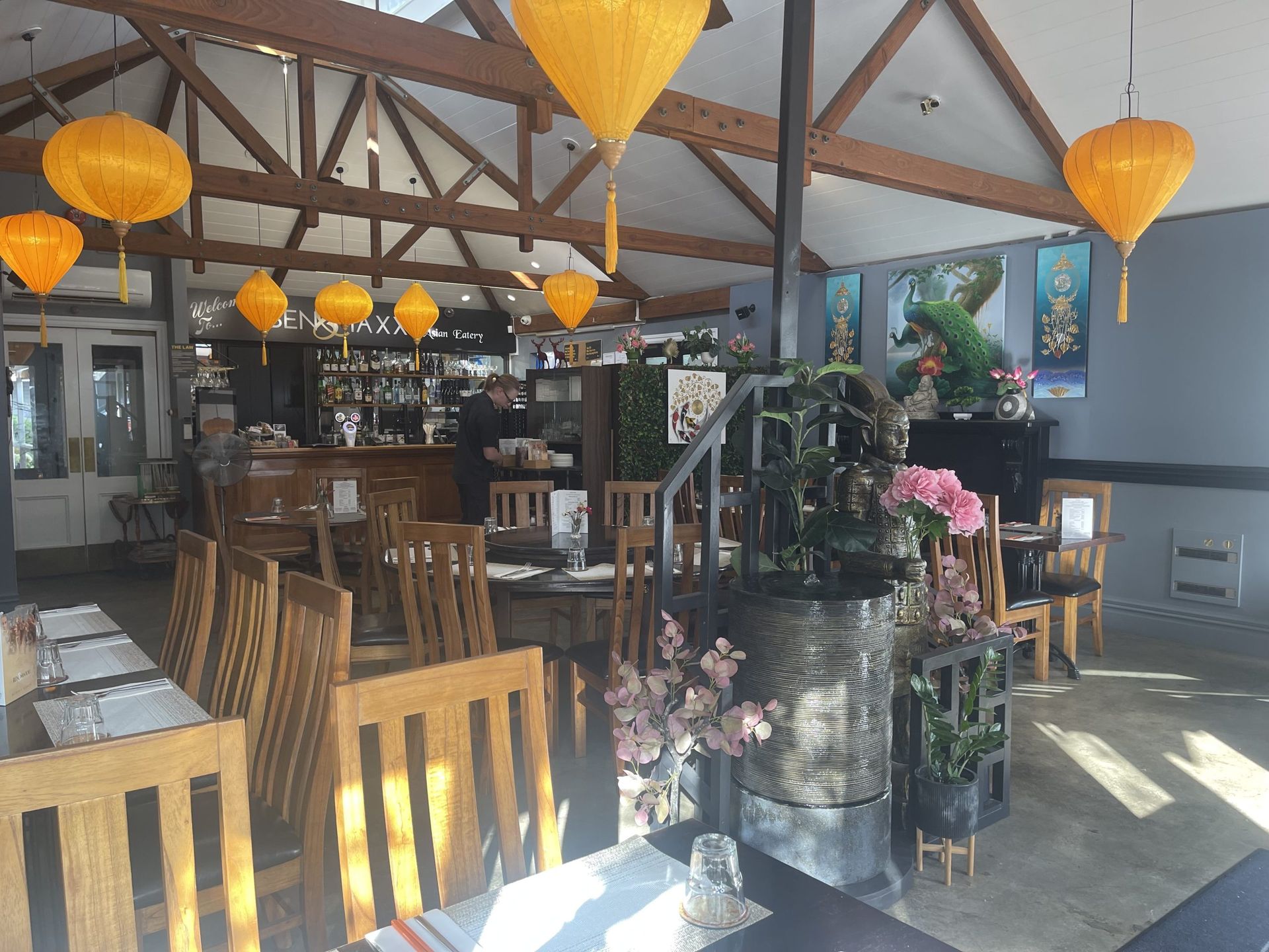 A restaurant with tables and chairs and yellow lanterns hanging from the ceiling.