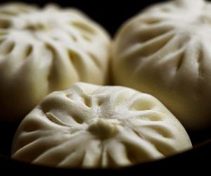 Three white dumplings are sitting on top of each other on a black surface.