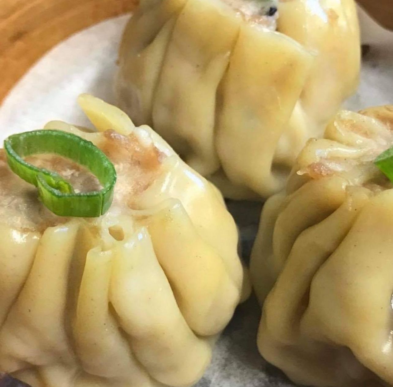 A close up of three dumplings with green onions on a plate.