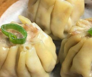 A close up of a plate of dumplings with green onions on top.