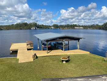 A dock with a covered boat slip on a lake with a blue sky and scattered clouds.