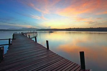Wooden pier extends over calm water toward a colorful sunset.