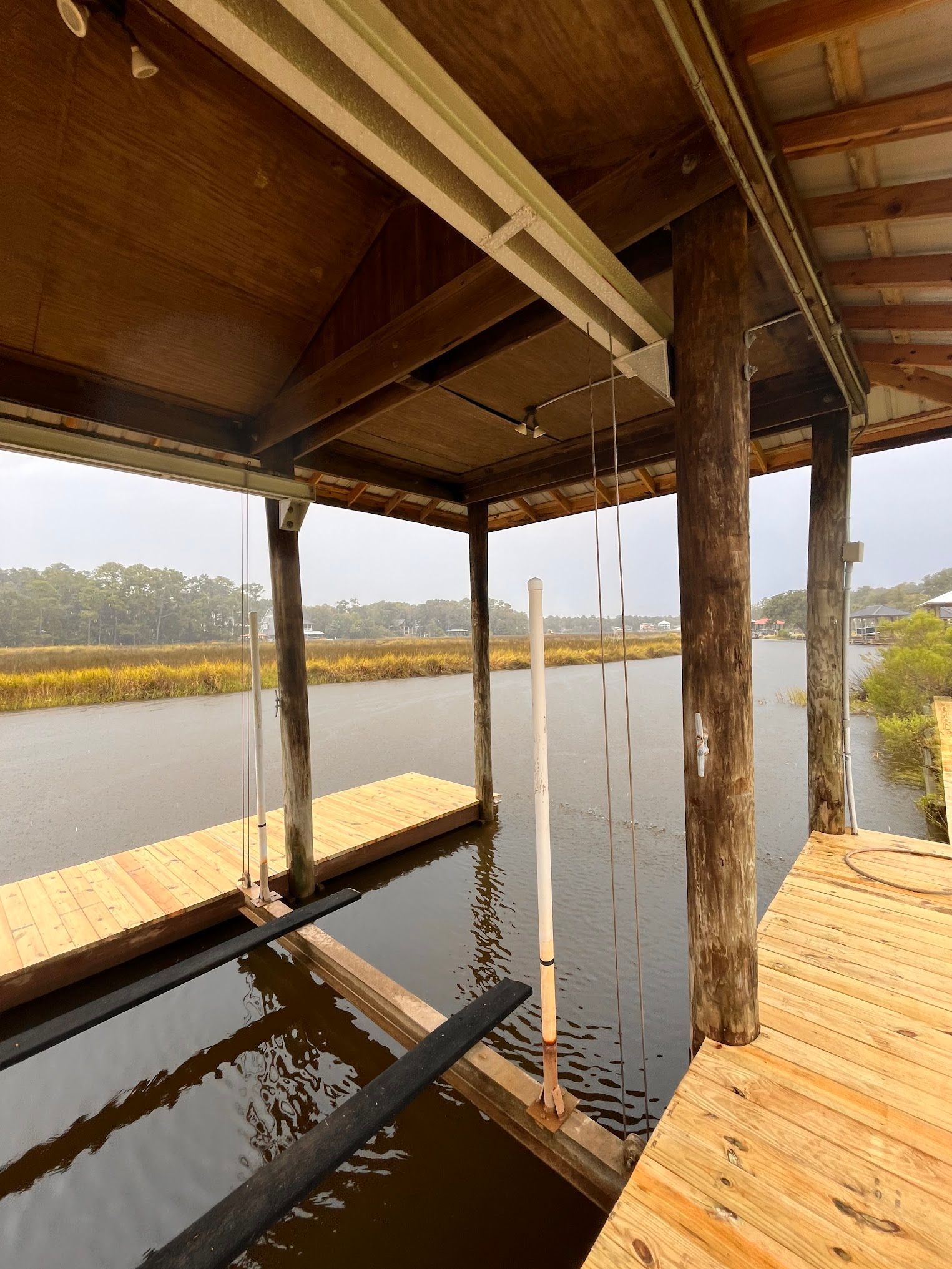 Wooden boathouse over a waterway with a dock, supports, and a covered roof.
