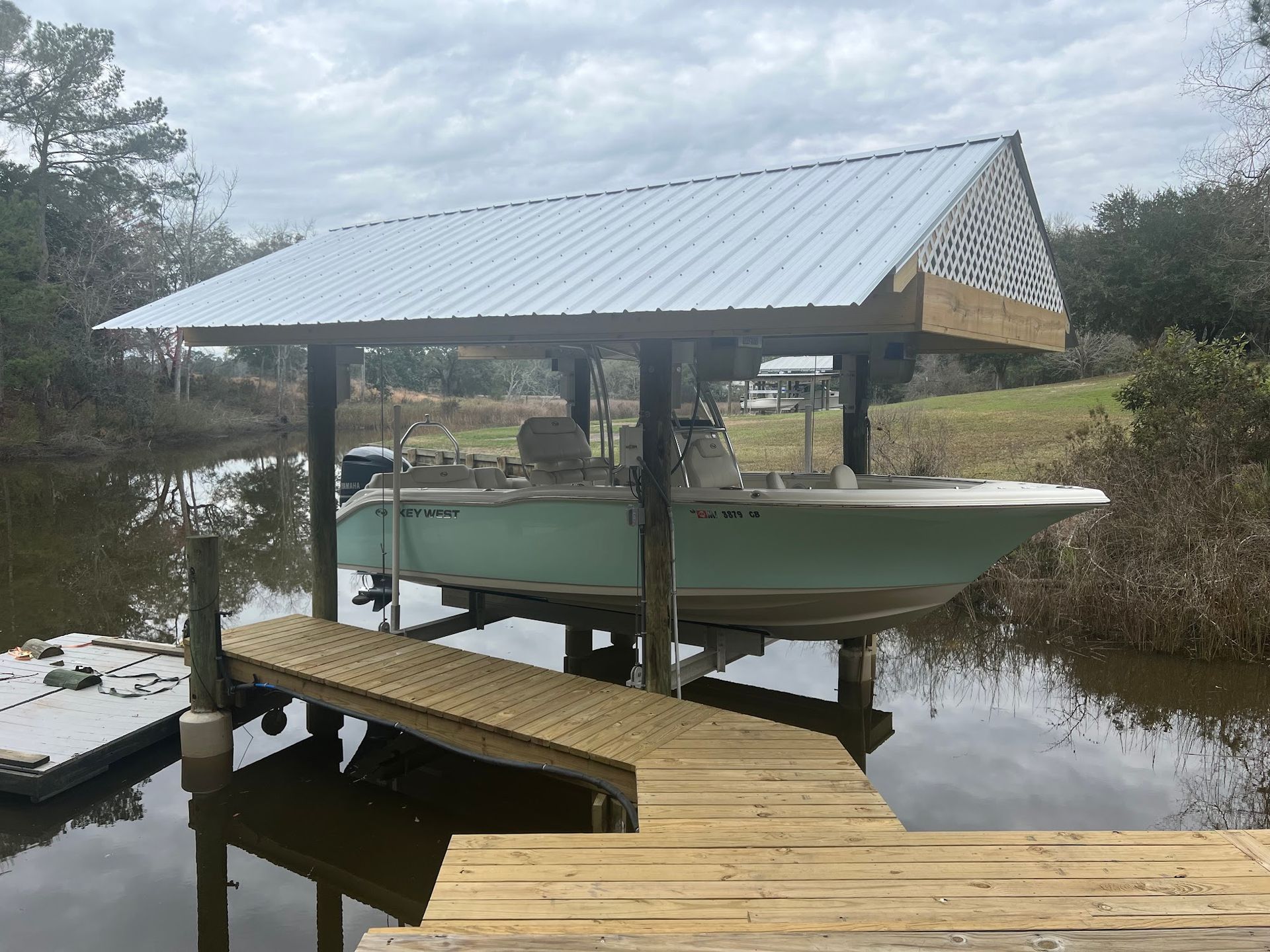 Boat on a lift under a metal roof, next to a wooden dock.