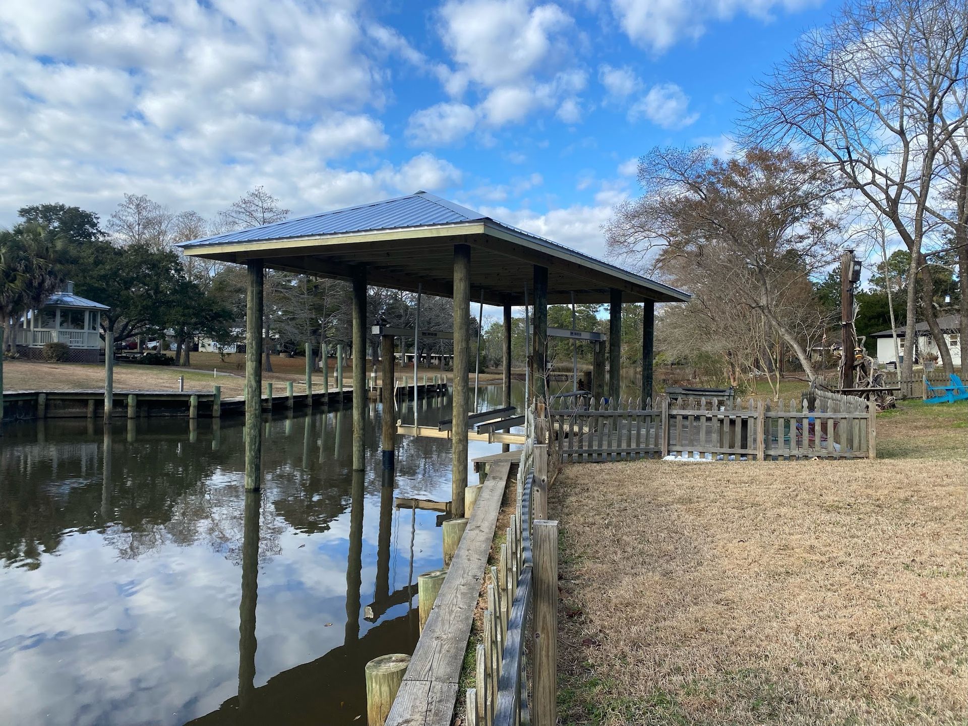 Dock with a covered boat slip on a canal. Blue sky, brown water, and wooden structures.