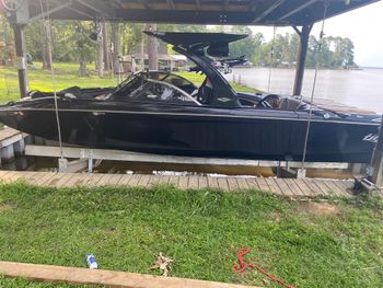 Black boat on a lift under a boathouse on a lake, green grass in foreground.