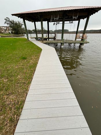 A concrete walkway leads to a covered dock on a lake. The sky is overcast.