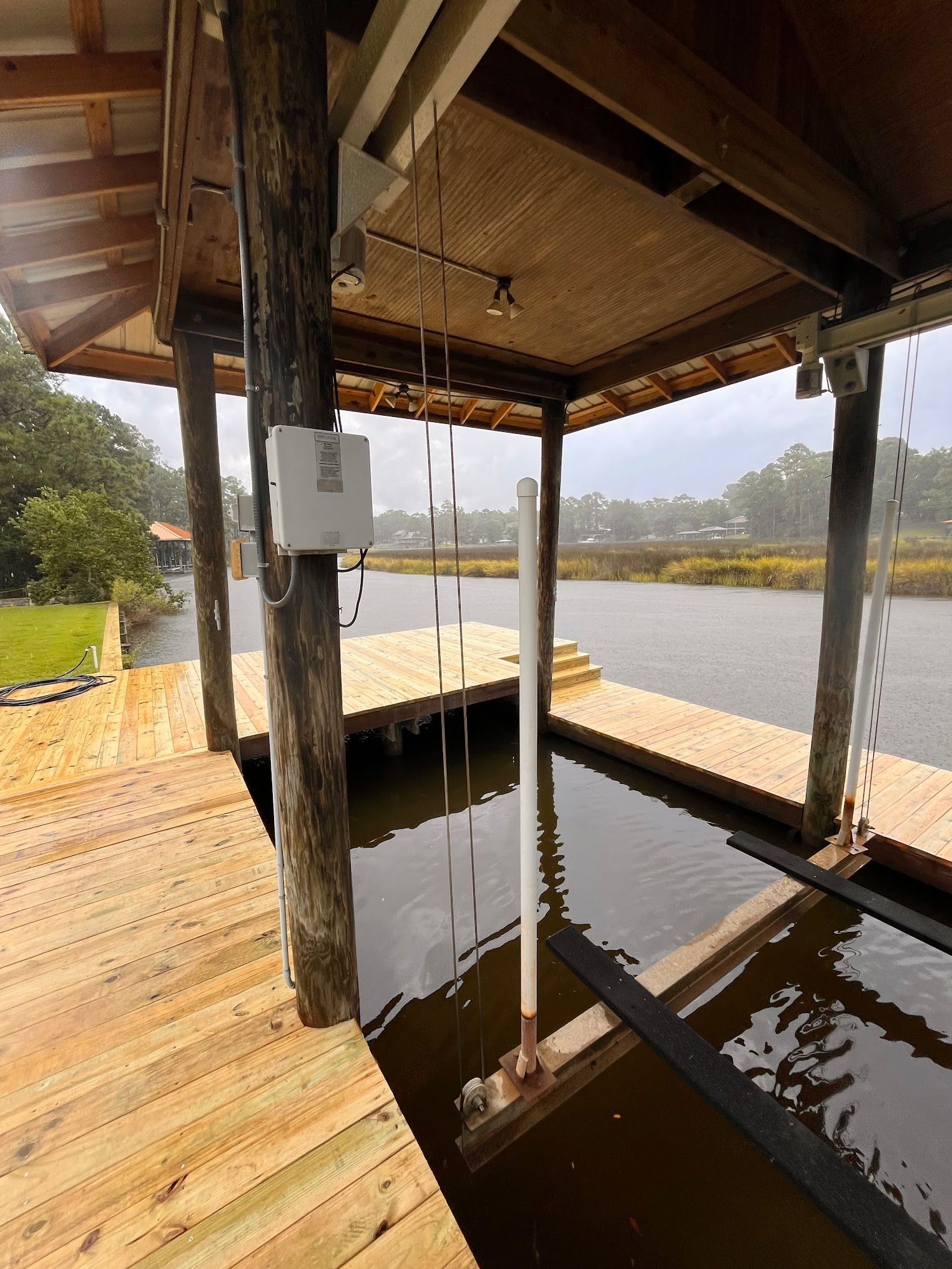 Wooden dock with boat lift over water, covered by a roof.