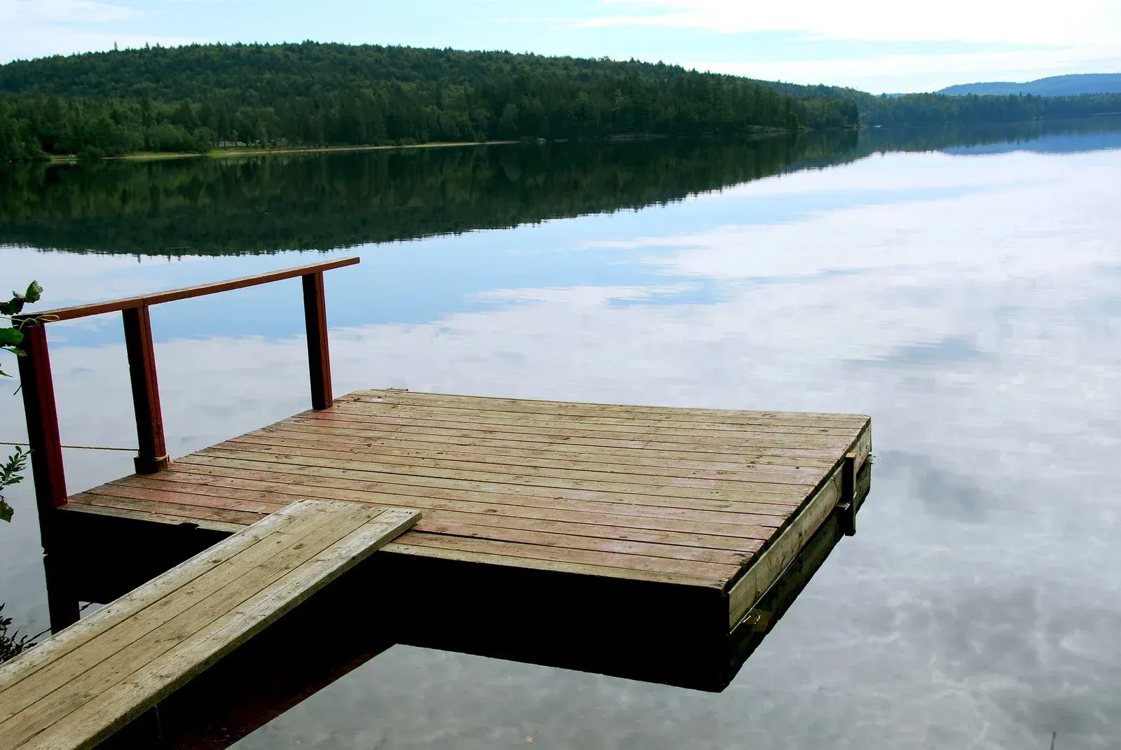 Dock on calm lake reflecting trees and sky.