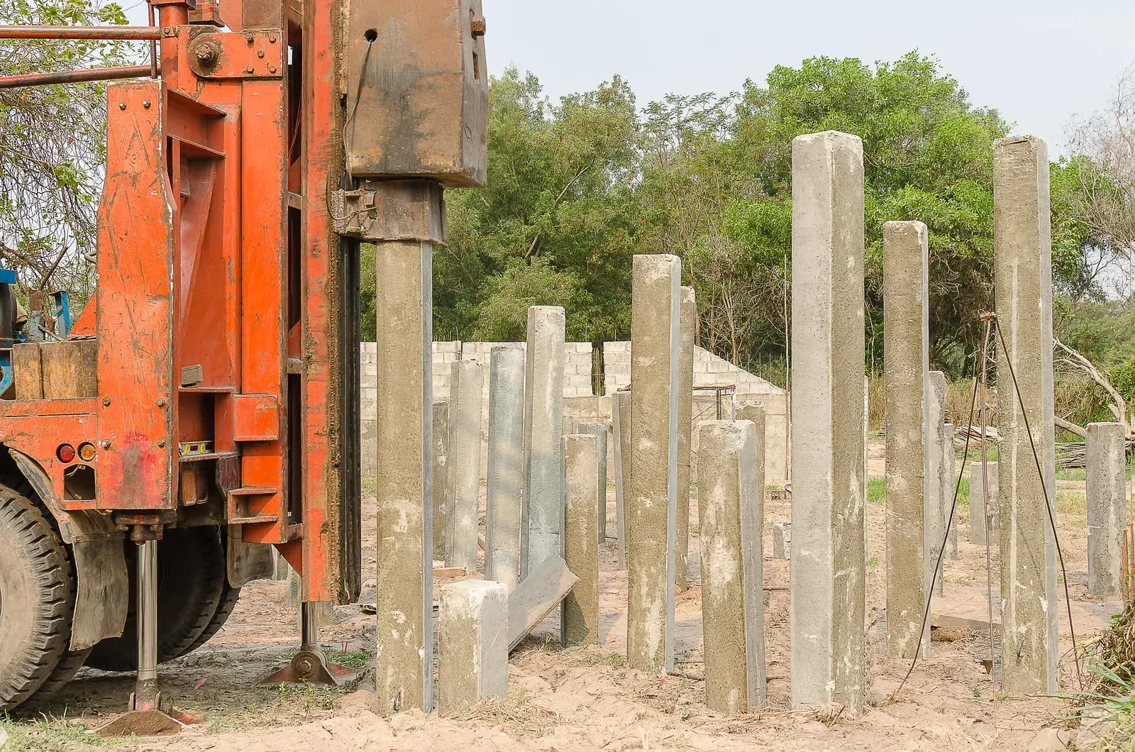 Orange construction machine driving concrete piles into the ground.