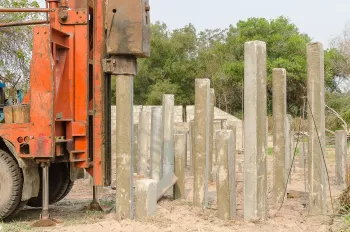 Orange construction machine driving concrete piles into the ground.