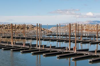 Empty boat docks in a marina, blue water, clear sky, distant mountains.