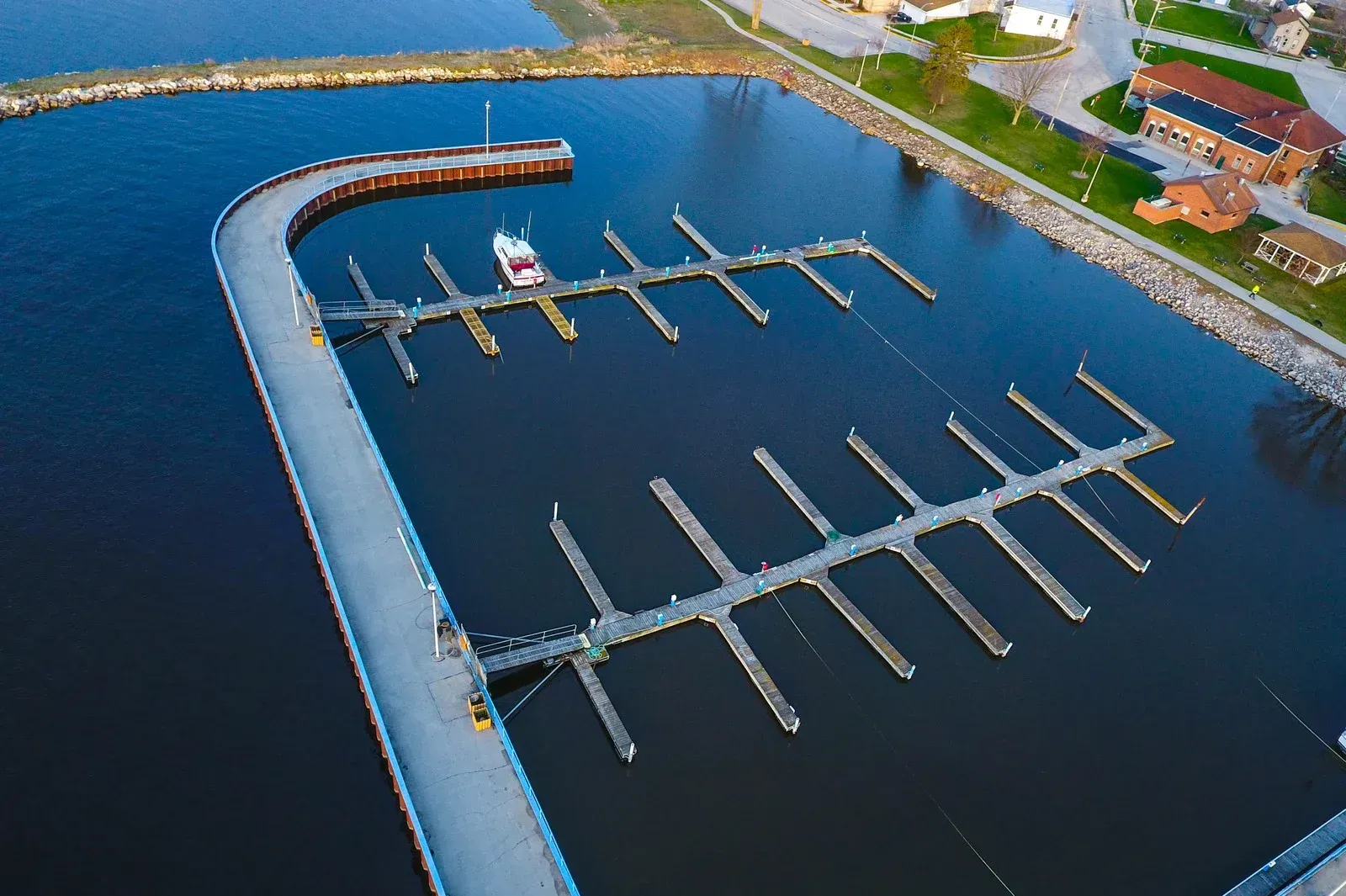 Aerial view of a marina with boat slips, pier, and a few boats. The water is dark, and the sky is overcast.
