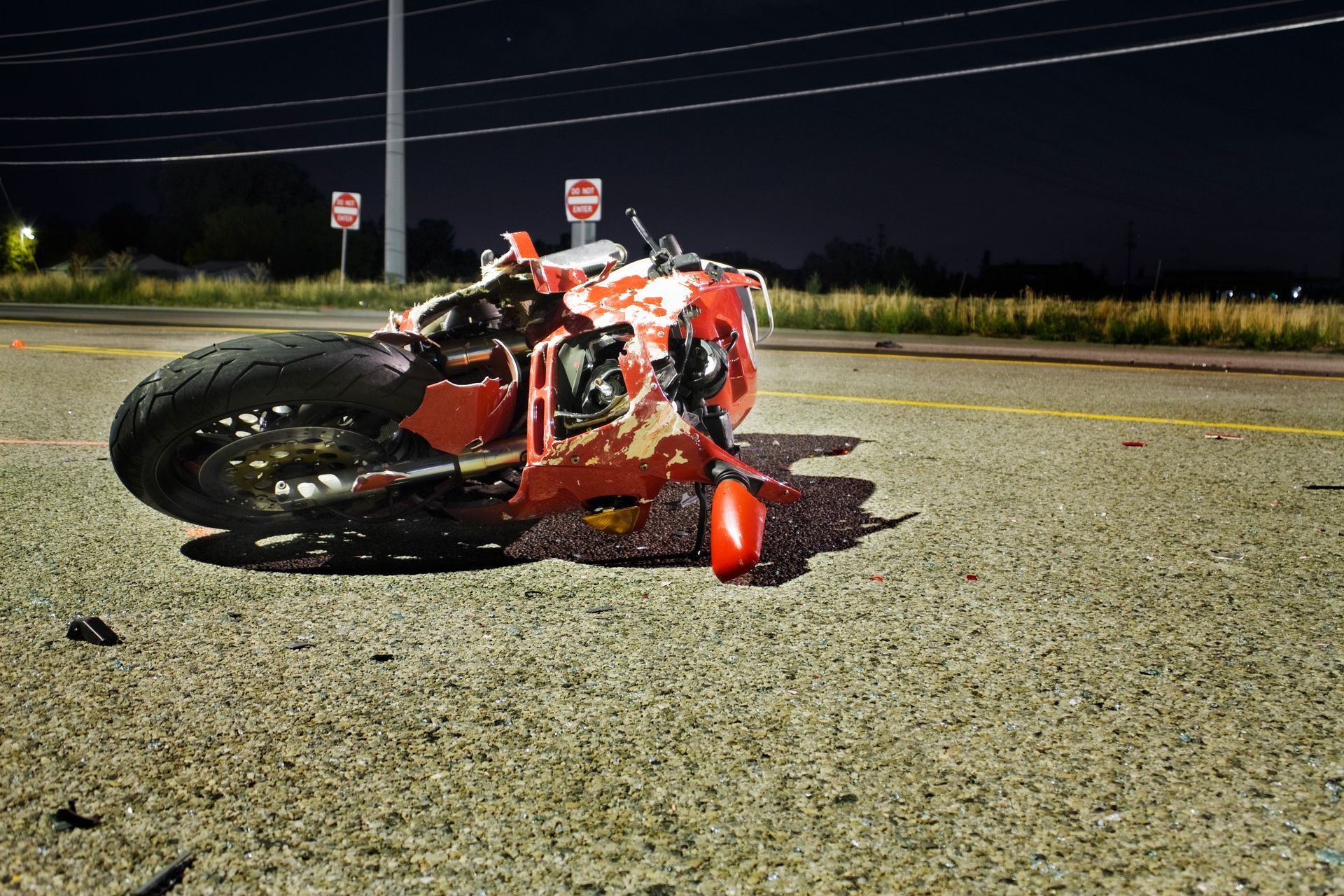 Nighttime motorcycle accident scene with damaged red bike on empty road.