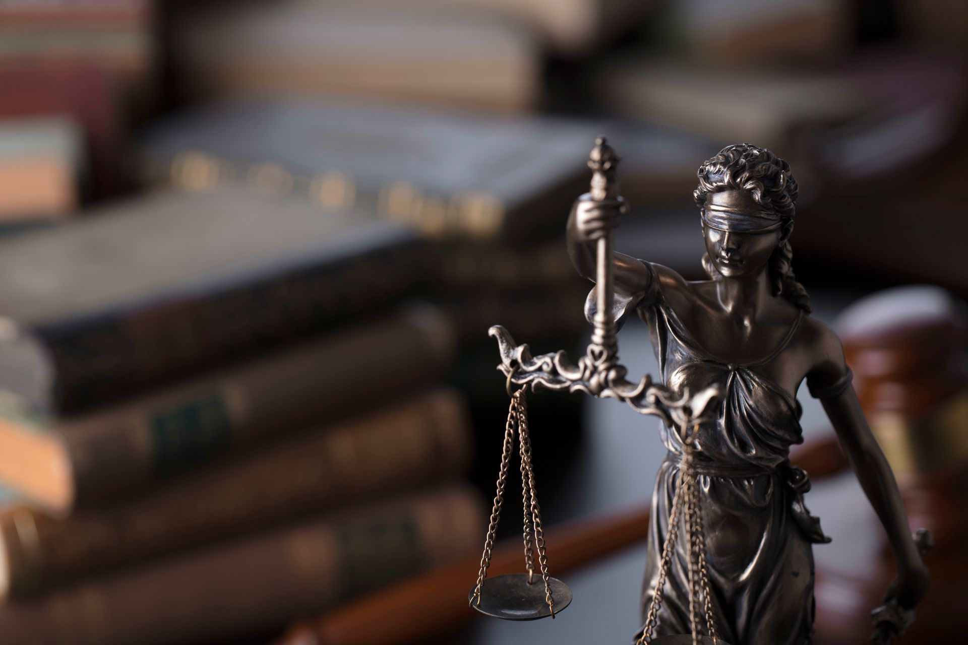 Lady Justice statue with scales in front of old law books, symbolizing legal fairness and justice.