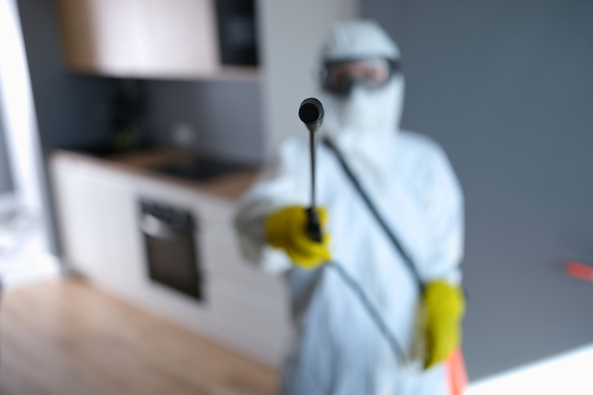 Person in protective suit holding a spray nozzle, possibly disinfecting a kitchen.