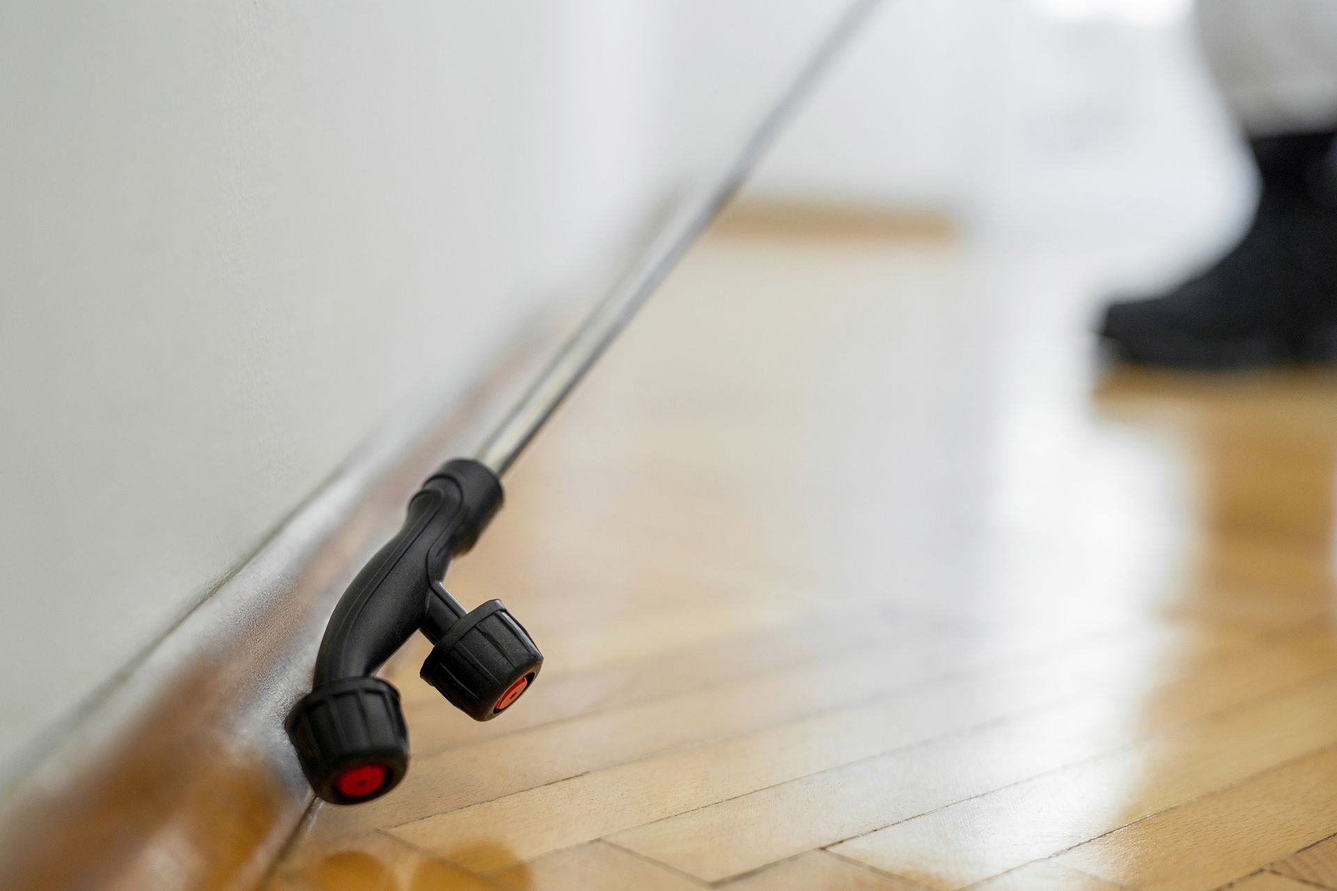 Pest control technician spraying insecticide along a wooden floor and wall baseboards.