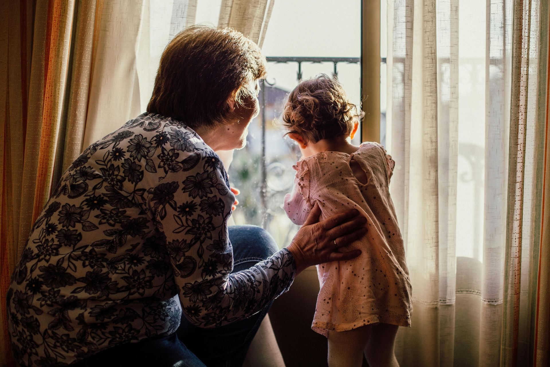 An elderly woman and a little girl are looking out of a window.