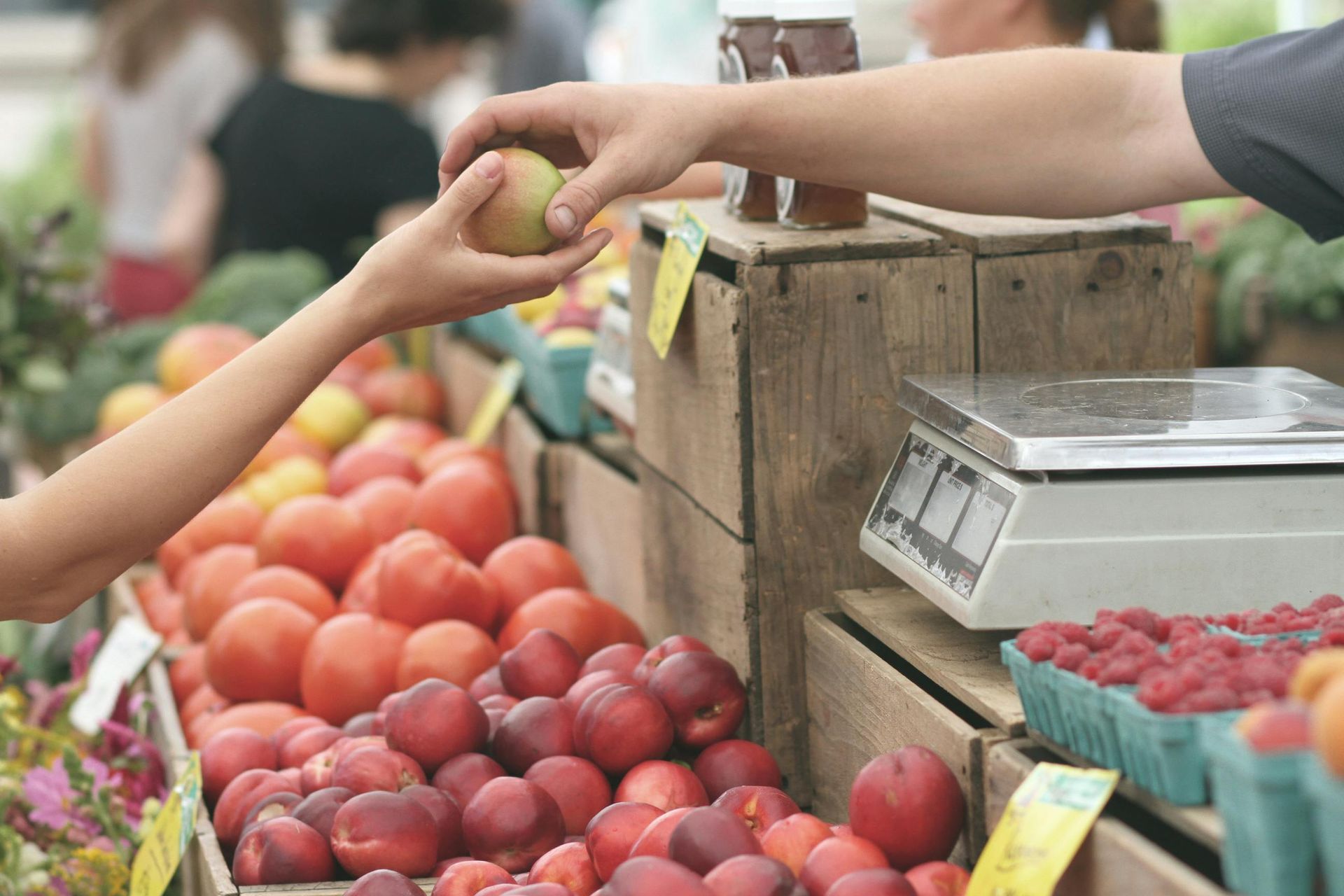 A person is reaching for an apple at a farmers market.