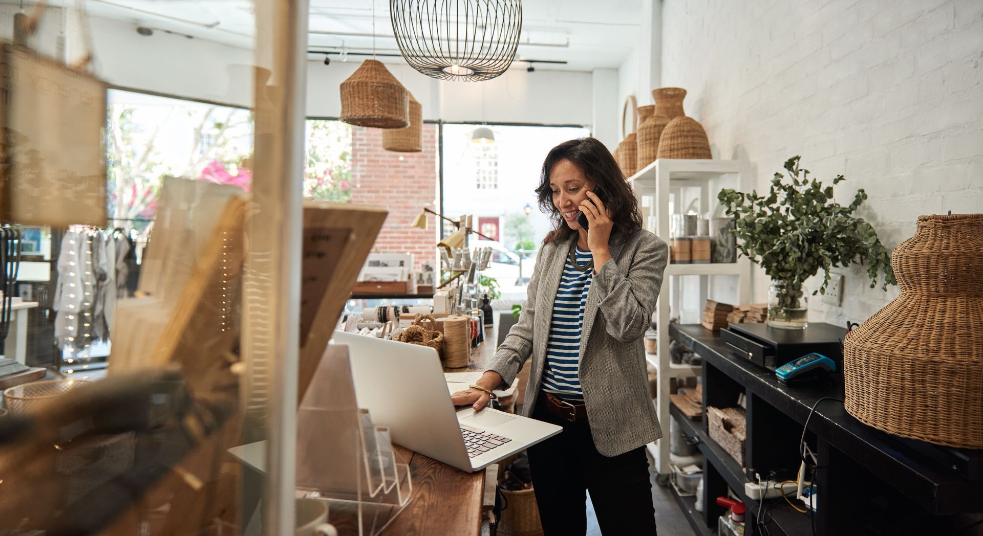 A woman is talking on a cell phone while using a laptop in a store.