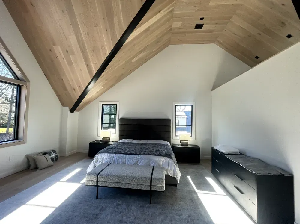 Bedroom with vaulted wood ceiling, white walls, and dark furniture.