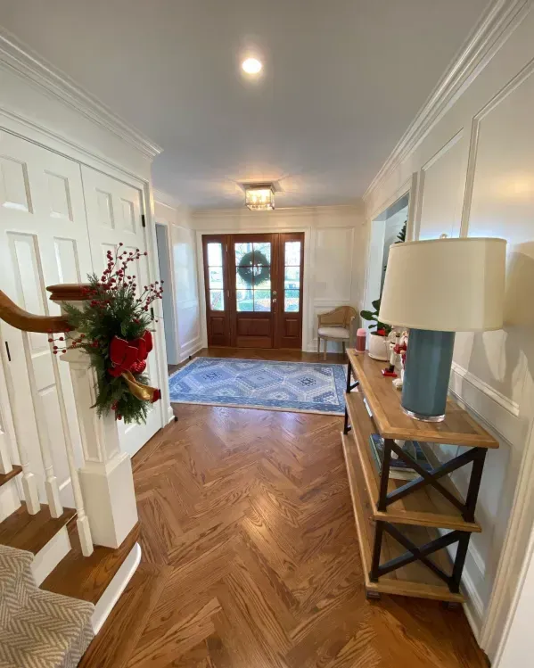 Entryway with herringbone wood floor, white walls, decorated with Christmas wreath and garland.