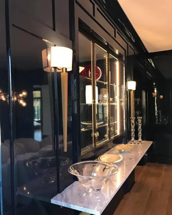 Black lacquered built-in cabinet with mirrored panels. Display table with crystal bowls. Two sconces provide light.