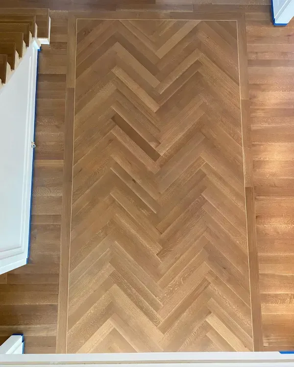 Herringbone pattern wooden floor with border, next to a staircase.