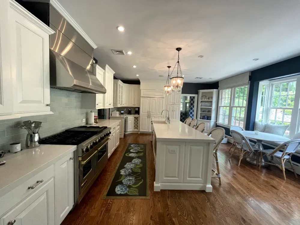 White kitchen with island, stainless steel appliances, dark wood floors.