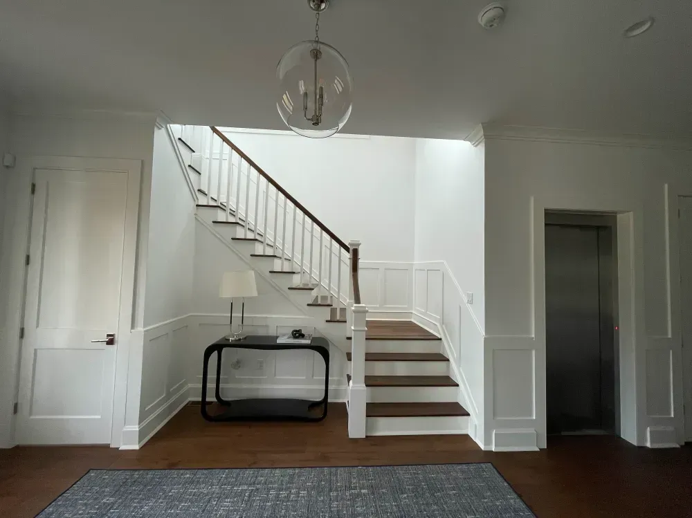 Interior view of a stairwell with stairs, elevator, and a small table with a lamp.