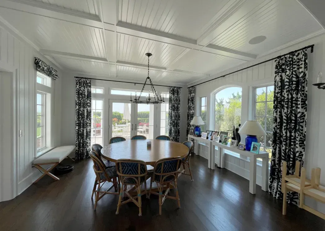 Spacious dining room with wooden table and chairs, hardwood floors, white walls, and patterned curtains.