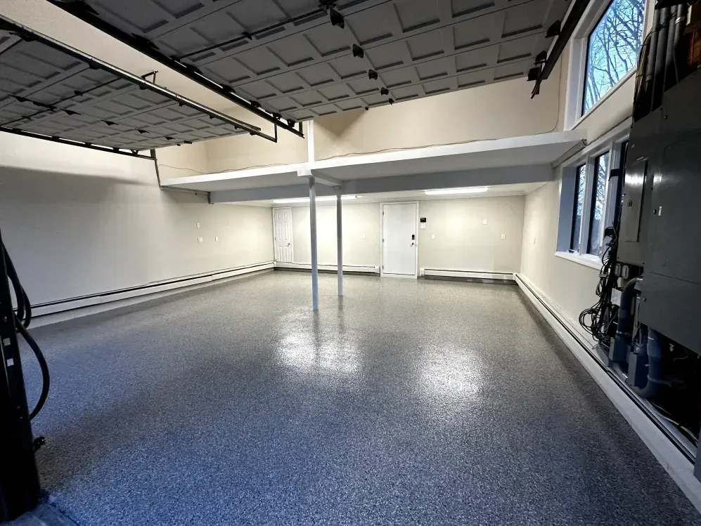 Empty garage with epoxy floor, white walls, overhead storage, and windows.