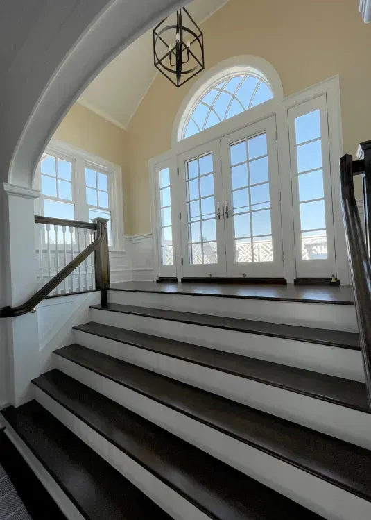 Interior staircase leading to a bright entryway with double doors, arched window, and a dark lantern.