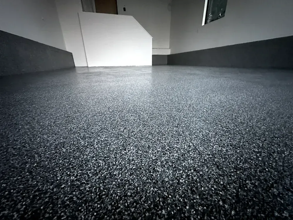 Epoxy-coated garage floor with dark gray speckled finish, white walls, and a small window.
