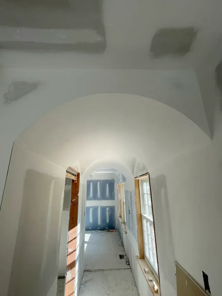 Hallway under construction with arched ceiling and window frames. Walls are primed white; drywall visible.