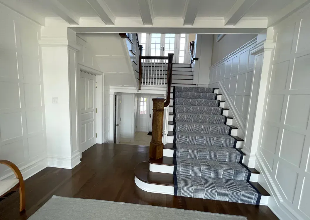 Spacious foyer with a staircase. White paneled walls, dark wood floors, and patterned stair runner.