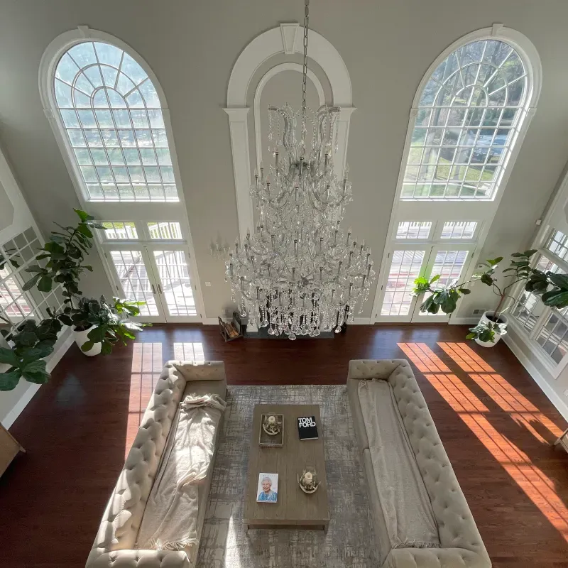 High-angle shot of a luxurious living room with a large chandelier, arched windows, and two tufted sofas.