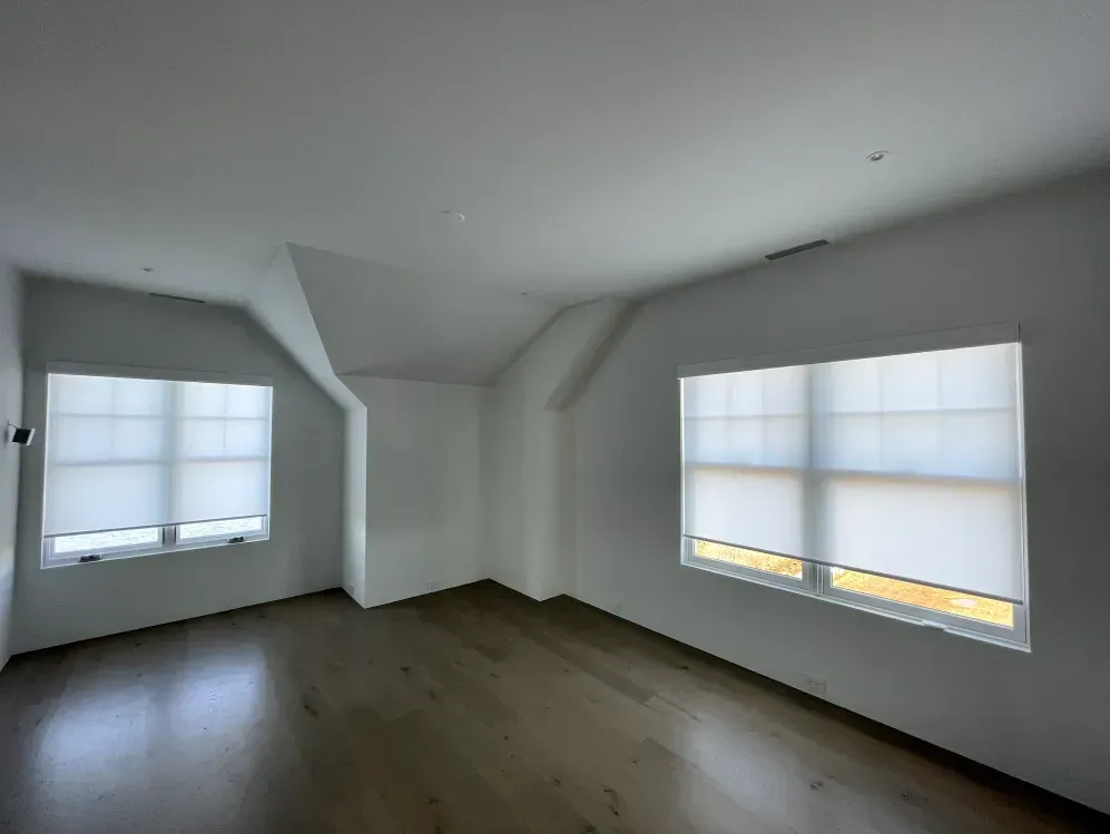 Empty room with hardwood floors, white walls, and two windows with blinds.