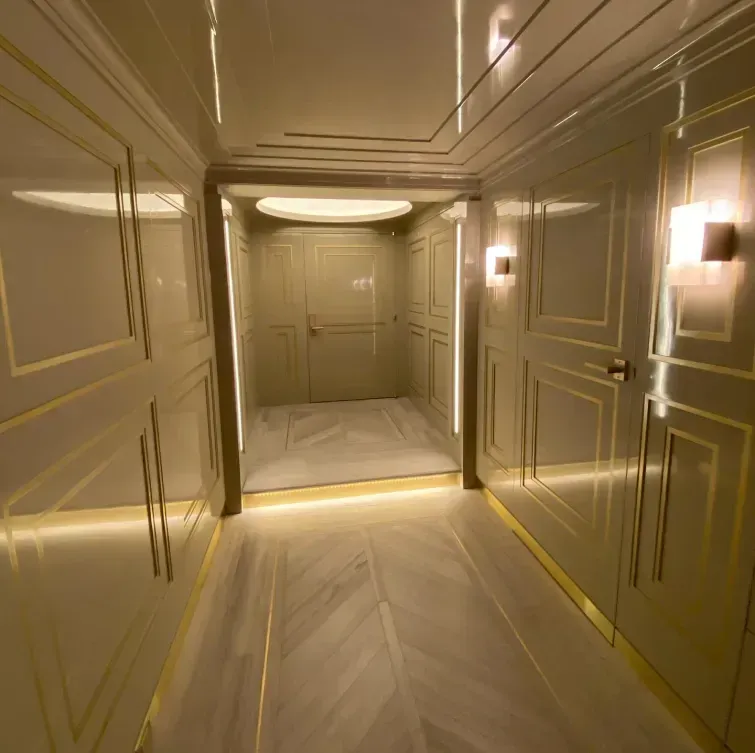Narrow hallway with light green walls, gold trim, and marble floor leading to double doors and a recessed ceiling light.