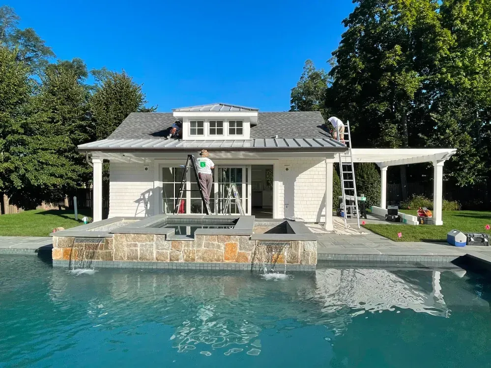 Workers on roof of white building by a pool on a sunny day.