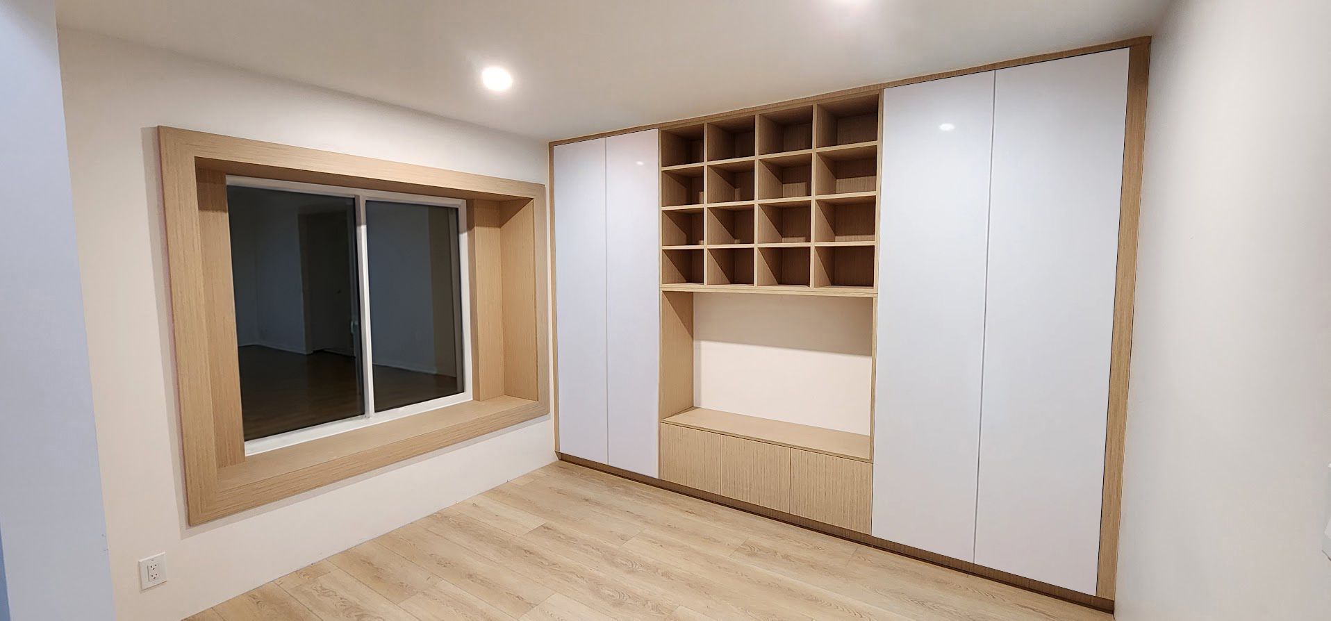 A room featuring a large window with a wood-trimmed frame, adjacent to a wall-to-wall storage unit with white doors.