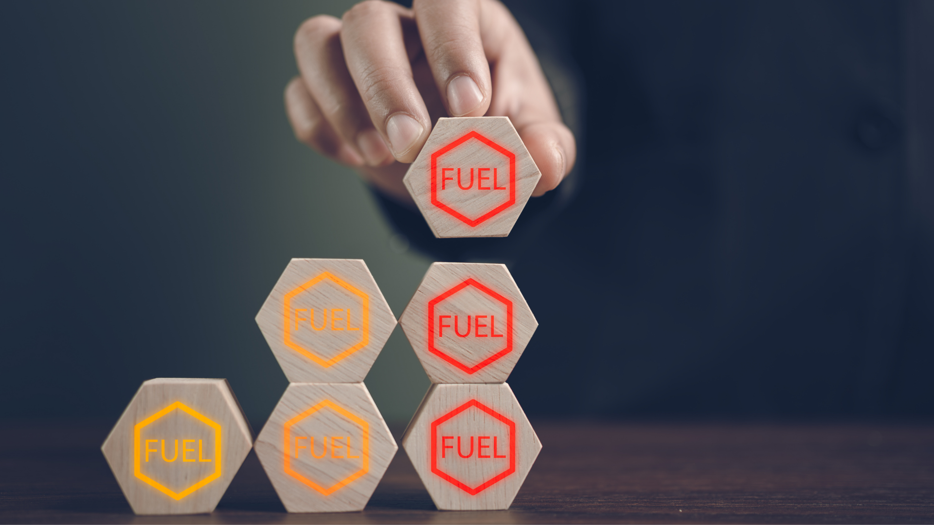 Hand stacking hexagon blocks labeled “FUEL” on a table against a dark background