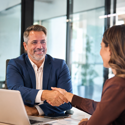 Two people shaking hands across a desk in a bright office