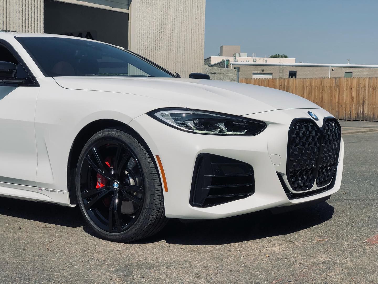 White BMW sports car with black rims, parked outside on a sunny day.